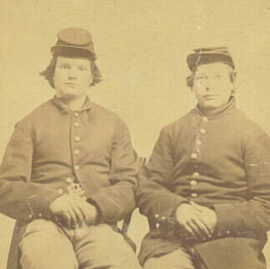 Two young men wearing uniforms and hats sitting in chairs