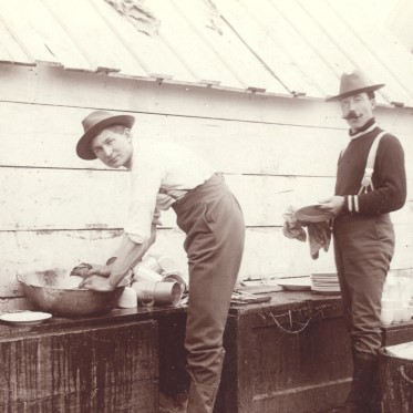 Two men standing beside a bench washing clothes